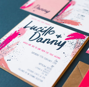 Square wedding invitation with slanted contemporary text saying 'Lucille & Danny', with a paint splash design in pinks and navy around the edges.